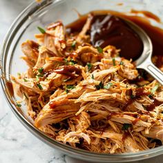 a glass bowl filled with shredded chicken and bbq sauce on top of a marble table