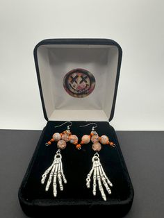 Embrace the spooky season with these Halloween dangling earrings that capture the essence of the holiday perfectly. Adorned with intricately designed skeleton hands and glass beads, each earring tells a whimsical tale of Halloween folklore. The lightweight yet eye-catching design ensures comfort while making a bold statement. Whether you're dressing up for a costume party or simply adding a touch of Halloween spirit to your ensemble, these earrings are the ideal accessory. Let these festive earrings be your playful companion throughout the Halloween season, adding a touch of macabre charm to any outfit. Celebrate the magic of Halloween with these unique, themed earrings that are sure to turn heads and spark conversations wherever you go. Drop Length: 3" Findings: Stainless Steel Witchy Halloween Earrings Adjustable, Witchy Adjustable Earrings For Halloween, Adjustable Witchy Earrings For Halloween, Halloween Dangle Metal Earrings, Metal Dangle Earrings For Halloween, Dangle Halloween Earrings, Witchy Metal Earrings For Halloween, Halloween Novelty Metal Earrings, Witchy Metal Halloween Earrings