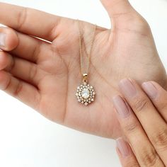 a hand holding a gold necklace with a white flower on the front and back of it