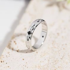 a white gold wedding ring with black diamonds on the inside and outside, sitting on a stone surface