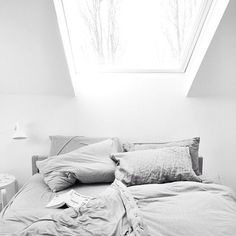 black and white photograph of an unmade bed in a room with slanted ceilings