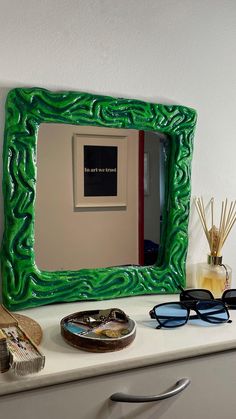 a green mirror sitting on top of a white counter next to a pair of glasses