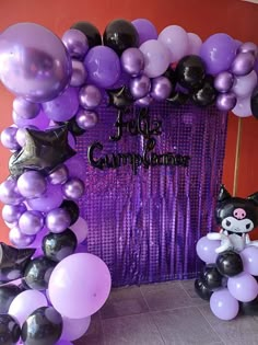 an arch made out of purple and black balloons with a cat sitting on the front