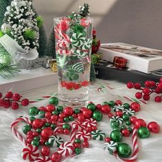 candy canes and candies are scattered around a glass vase on a white furnishing