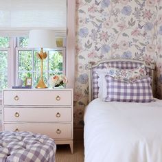 a bedroom with floral wallpaper and bedding in the foreground is a window