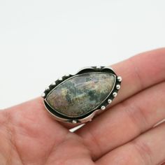 "This beautiful piece is handcrafted with exquisite detailing and features a genuine mottled blue-grey Agate stone that measures 1.5\" long and almost 1\" at its widest point. This measurement includes the solid sterling setting with its studded and gently curved ribbon-like design. The band fits a US size 10 finger and cannot be re-sized as the stone is already set (though you may order a custom ring). This ring is one of a kind and has matching earrings to go with it. The earrings measure 1.25 Unique Jasper Ring Jewelry, Artisan Jasper Teardrop Jewelry, Moss Agate Jewelry With Large Round Stone, Handmade Earthy Silver Jewelry, Handmade Gray Round Jewelry, Earthy Handmade Silver Jewelry, Unique Moss Agate Jewelry With Natural Stones, Adjustable Moss Agate Gemstone Jewelry, Bohemian Moss Agate Gemstone Jewelry