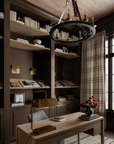 a desk with a lamp and bookshelf in the corner next to a window