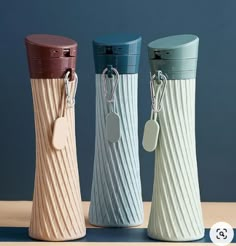 three different colored vases with tags attached to the handles and sides, on a table