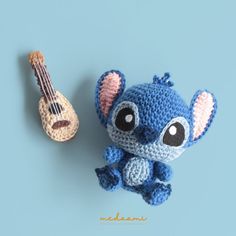 a crocheted blue stuffed animal next to a ukulele on a blue background