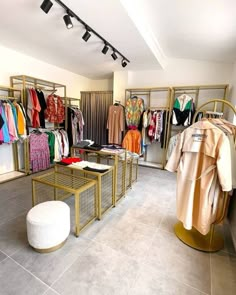 the inside of a clothing store with clothes on racks and stools in front of them