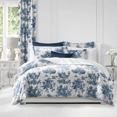 a bed with blue and white comforters in a bedroom next to a window filled with flowers