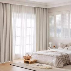 a bedroom with white walls and wooden flooring, large window coverings on the windows