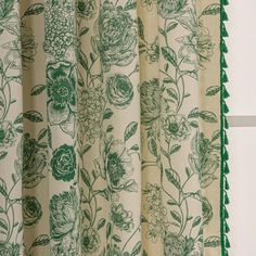 a curtain with green flowers and fringes hanging from it's side, in front of a white wall