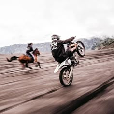 two people are riding motorcycles on the dirt road while another person is running behind them