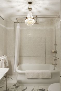 a bathroom with a chandelier hanging from the ceiling and marble tile flooring