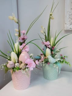 two vases filled with flowers on top of a white table next to a mirror