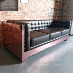 a black leather couch sitting in front of a brick wall next to a book shelf