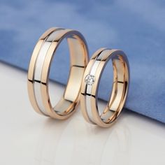 two gold wedding bands with a diamond in the middle and one on each side, sitting next to each other