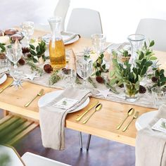 the table is set with pine cones, greenery and silverware