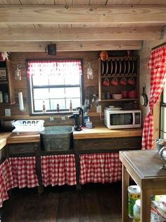 a kitchen with red and white checkered tablecloths on the counter top, sink, oven, microwave and window