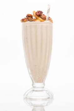 a smoothie in a tall glass with a straw and some nuts on the top