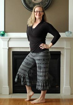 a woman standing in front of a fireplace with her hands on her hips and legs crossed