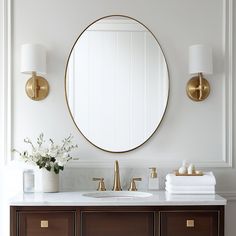 a bathroom vanity with a round mirror and gold faucet on the wall above it