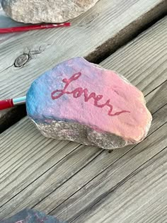 a rock with the word love painted on it sitting on a wooden surface next to scissors