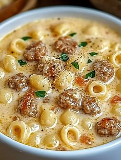 a bowl of soup with meatballs and cheese in it on a table next to bread