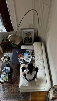 a woman sitting on top of a white couch in a living room next to a window