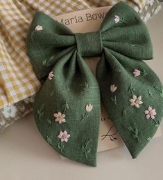 a green bow with pink flowers on it sitting on top of a white and yellow checkered table cloth