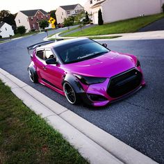 a pink sports car parked on the side of the road in front of some houses