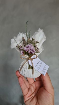 a hand holding a small white bag with flowers in it and a tag attached to it