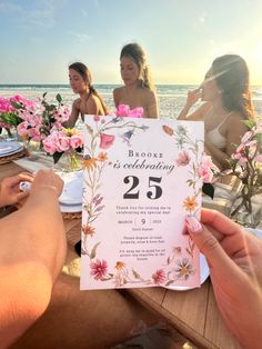 people sitting at a table with flowers on it and one person holding up a card