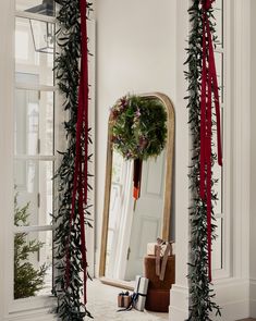 a christmas wreath is hanging on the wall in front of a mirror with red ribbon