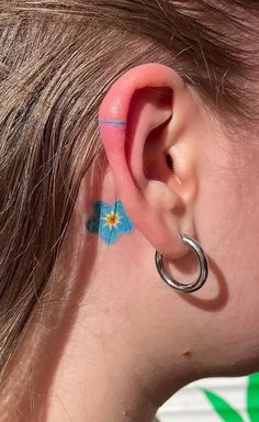 a woman with blue flowers on her ear and behind the ear is a pair of silver hoop earrings