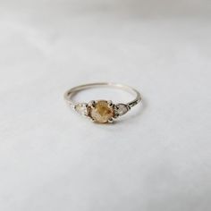 a close up of a ring on a white surface with an orange stone in the middle