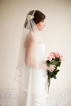 a woman in a wedding dress holding a bouquet of flowers and wearing a veil over her head