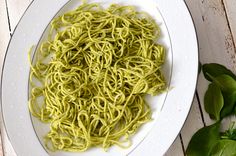 a white plate topped with green noodles next to some leaves on top of a wooden table