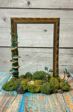 a moss covered frame sitting on top of a wooden table next to rocks and mushrooms