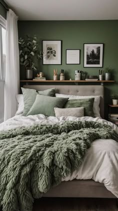 a bed with green blankets and pillows in a bedroom next to a window filled with potted plants