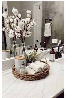 a bathroom counter with a basket filled with cotton flowers and towels on top of it