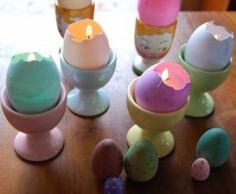 there are many different colored eggs on the table with one candle in the egg cup