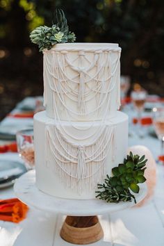 a three tiered white wedding cake with succulents and greenery on top