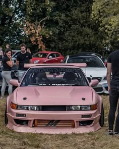 two men standing next to pink cars in a field