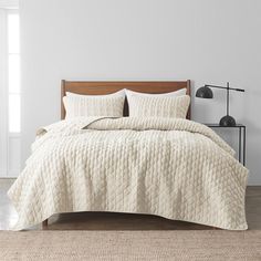 a bed with white bedspread and pillows in a room next to a lamp