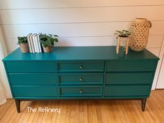 a green dresser with two books on top and some potted plants next to it