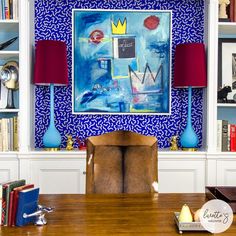 a painting on the wall above a wooden table with two lamps and bookshelves