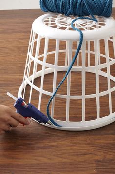 a person using a crochet hook to attach a piece of yarn on top of a white wire basket