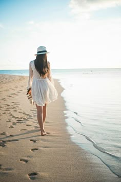 a woman is walking on the beach with her hat in hand and footprints in the sand